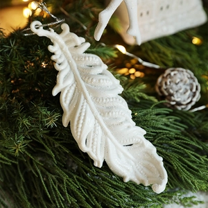 White feather Christmas ornament with silver glitter on green pine branches