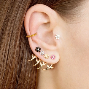 Macro detail of layered gold floral stud earrings and colorful gemstone ear cuffs set