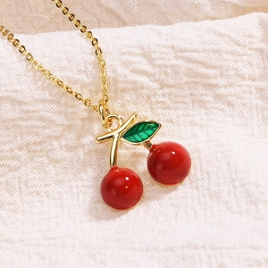 Golden necklace with vibrant red hand-painted cherry pendant on white textured fabric