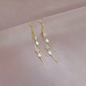 Detail of long gold tassel earrings with rhinestone flowers and oval pearls on satin