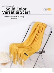 Detail shot of a warm ginger yellow cashmere scarf with fringe on a modern chair