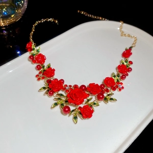 Macro view of gold chain necklace featuring red rose floral pendant and green leaves