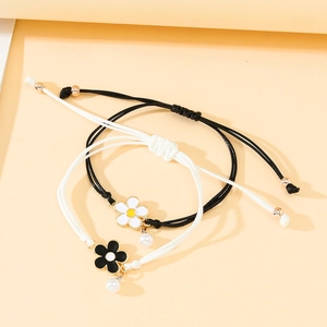 Detail of woven bracelets with enamel daisy charms and small pearls in black and white
