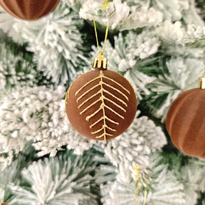 Détail de boules de Noël en velours marron avec motifs pailletés dorés sur branches enneigées