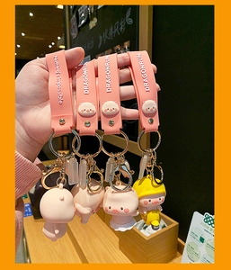 Close-up of cute cartoon pig keychains with silicone straps and metal rings held in hand