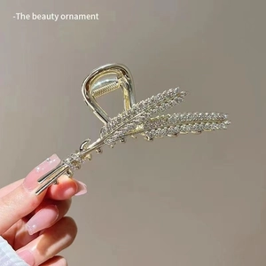Detail of a golden wheat-shaped hair claw clip with sparkling rhinestones for women