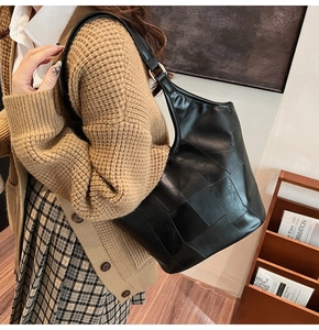 Detail van een zwarte leren tote bag met geometrische stiksels en metalen gesp op de schouder
