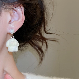 Close-up of a white flocked puppy earring with a pearl stud on female model ear