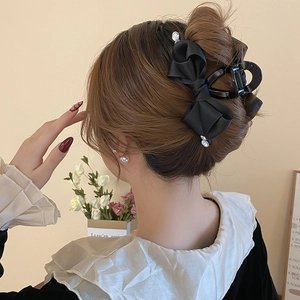 Detail of a black satin bow hair claw clip with pearl embellishments on model hair
