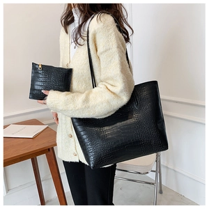 Set of large black crocodile-patterned tote bag and clutch shown on a model in a cozy room