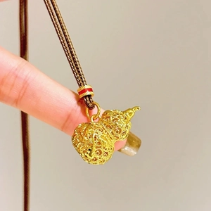 Close-up of a 24k gold-plated filigree gourd pendant on a brown woven necklace cord