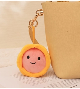 Porte-clés peluche tarte aux œufs avec visage souriant sur un sac à main en cuir beige