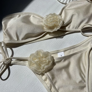 Detailed view of champagne satin bikini fabric with 3D floral accents and size S label