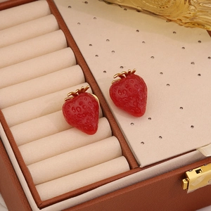 Cute strawberry stud earrings in red and gold finish on a leather jewelry box