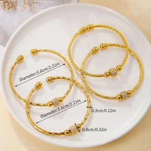 Detailed view of four golden bangles with fine engraved texture and zircon accents