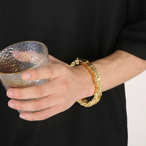 Detail of a gold industrial chain bracelet on wrist holding a textured glass