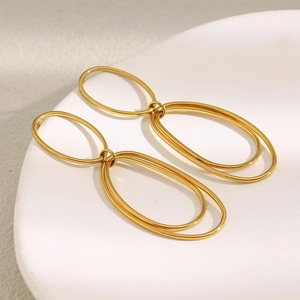 Macro shot of gold-plated geometric oval earrings resting on a white ceramic plate