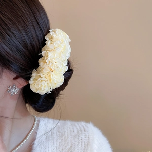 Close-up of elegant cream fabric flower hair pin worn on a textured side bun hairstyle