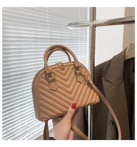 Close-up of beige quilted shell bag with V-shaped stitching and metal zipper detail