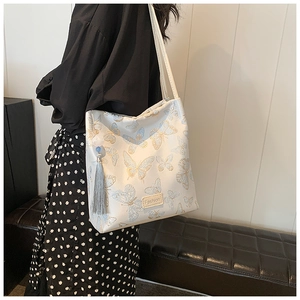 Detail of cream tote bag with blue butterfly print, tassel charm, and leather Fashion label