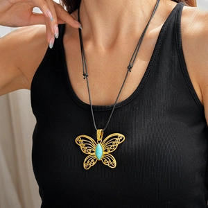 Close-up of golden hollow butterfly pendant necklace with turquoise stone on black cord