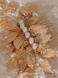 Close-up of golden leaf hair comb with elegant white pearls on beige fabric background