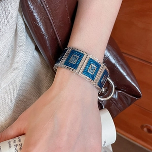 Close-up of a silver wide cuff bracelet with blue enamel squares and spiral textures