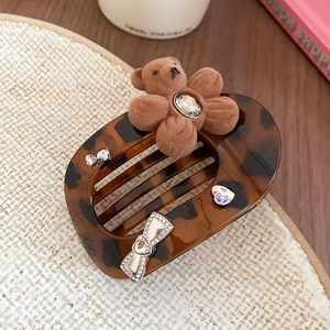 Detail of tortoise shell hair claw clip featuring a plush bear and rhinestone bow