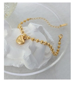 Macro detail of 18K gold-plated beaded bracelet with heart pendant and lobster clasp