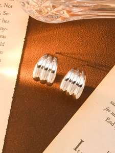 Detailed close-up of chunky silver C-shape textured metal earrings in a lifestyle setting
