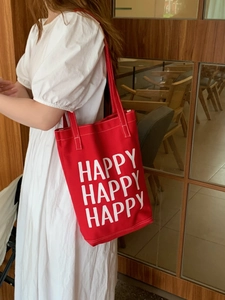 Close-up of a red canvas shoulder bag with happy text print worn with a white dress