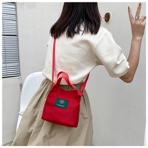 Detail of red canvas bucket bag with green label shown in a lifestyle side view