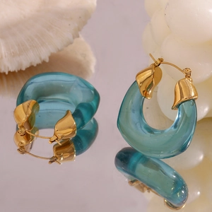 Close-up of gold U-shaped earrings with blue acrylic charms on a mirror background