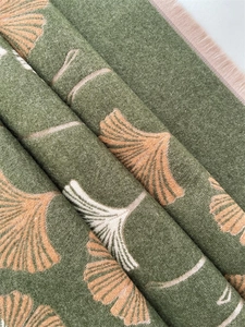 Close-up of green cashmere-feel scarf showing orange ginkgo leaves and soft fabric texture