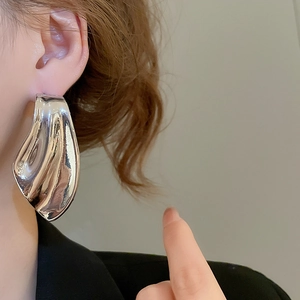 Close-up of large irregular silver fishtail earring on model showing metallic texture