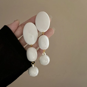 Detail of long white acrylic earrings with gold links held by hand against beige background
