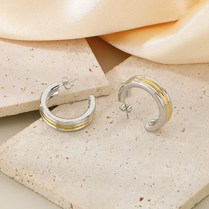Detail view of two-tone gold and silver C-shaped hoop earrings on silk background
