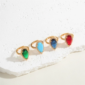 Adjustable gold rings with emerald and ruby pear-cut gemstones set on stone background