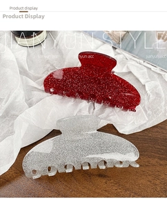 Close-up of glitter acrylic hair claws in red and silver on a textured surface