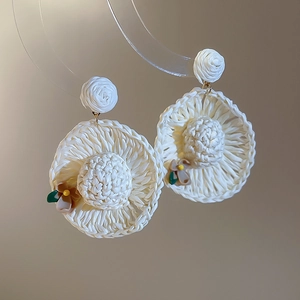 Close-up of woven straw hat earrings with rose stud and small flower detail