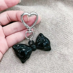 Detail of a glossy black bow keychain with a silver heart-shaped metal clasp