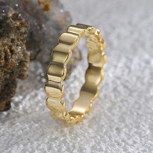 Close-up of a minimalist golden wavy textured ring with a scallop-edged design on white stone