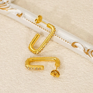 Gold rectangular hoop earrings with white rhinestones on a textured beige background