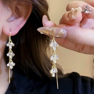 Detail view of long tassel gold earrings featuring leaf-shaped crystals and fine metal chains