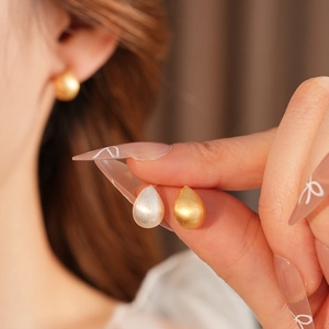 Close-up of minimalist teardrop earrings in matte gold and silver finishes on a model