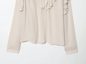Close-up of ruffled neckline and soft fabric texture on a beige long-sleeve blouse