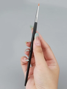 Close-up of fine tip eye makeup brush with orange bristles for precision eye detailing