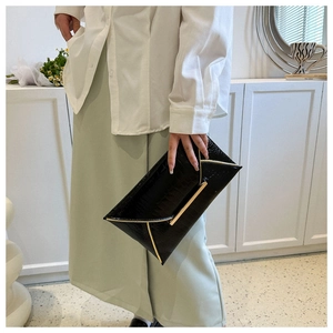Detail of black envelope clutch with gold V-shaped metal trim and crocodile leather texture