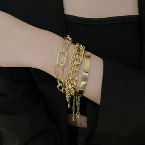 Detail of four-piece layered gold chain bracelet set worn over a black suit sleeve