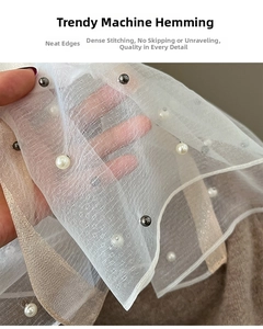 Close-up of white mesh shawl with pearl beads and machine-stitched edges detailing